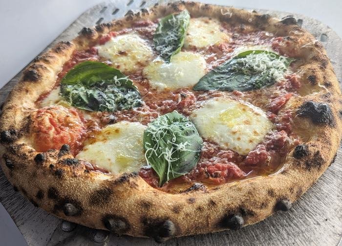 A Margherita pizza with fresh basil and mozzarella on the peel