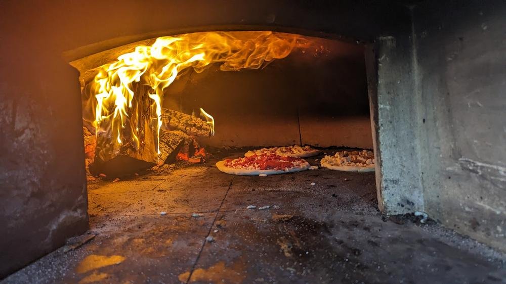 Raw pizzas on the oven floor beside a tall flame