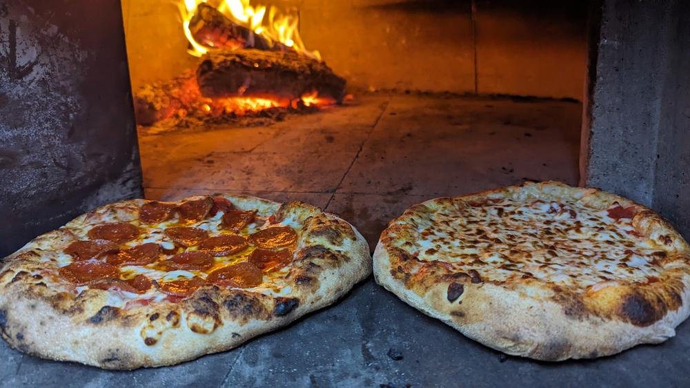 Two finished pizzas on the oven floor with the fire behind them
