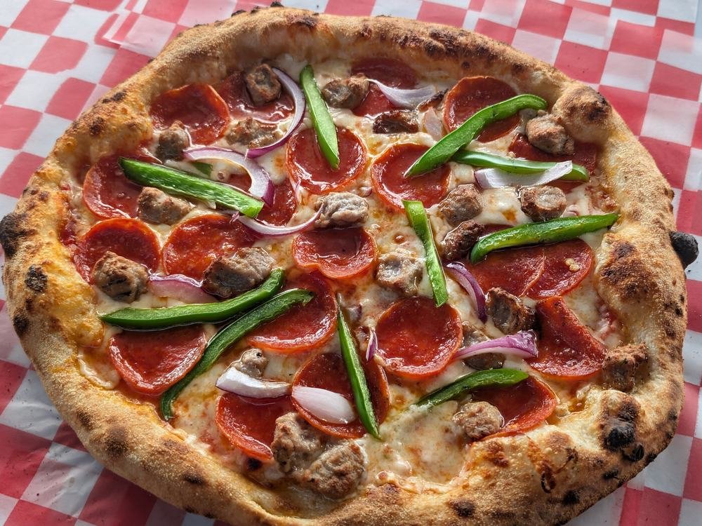A pepperoni, sausage, pepper and onion pizza on red check paper